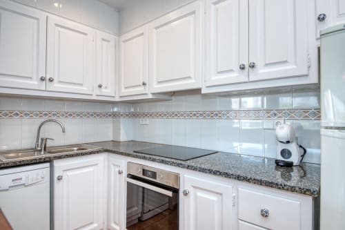 Cuina moderna blanca amb encimeres de granit, electrodomèstics d'acer inoxidable i recobriment de rajoles decoratives a Ancora