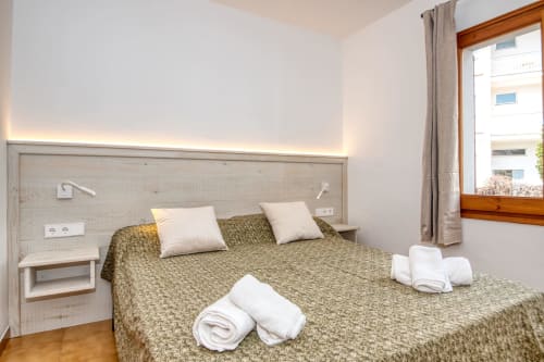 Dormitori modern i lluminós a Finques Garcia Enrich de Palafrugell amb cobrellits verd, coixins blancs i capçal de fusta