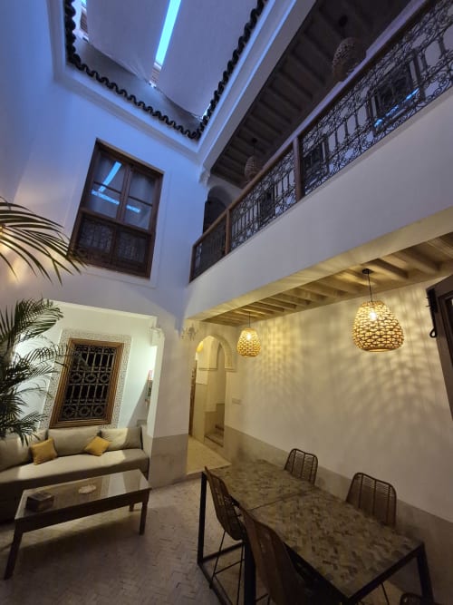 Cour du Riad Casa Angelo à Marrakech avec coin détente, table à manger, luminaires suspendus et architecture traditionnelle