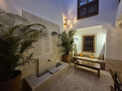 Cour du Riad Casa Angelo à Marrakech avec carrelage zellige raffiné, plantes de palmier, coin détente et décor traditionnel