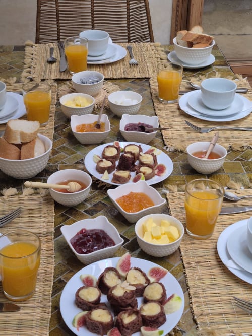 Petit-déjeuner marocain au Riad Casa Angelo avec pâtisseries, confitures, fruits frais et jus d'orange sur une table de salle à manger en plein air
