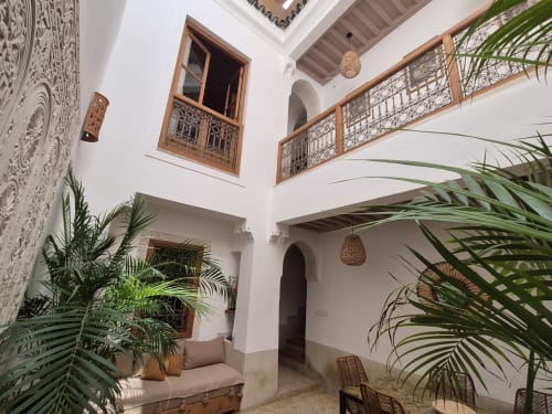Patio du Riad Casa Angelo à Marrakech avec murs blancs, fenêtres en bois sculptées, balustrades ornées et tissages suspendus