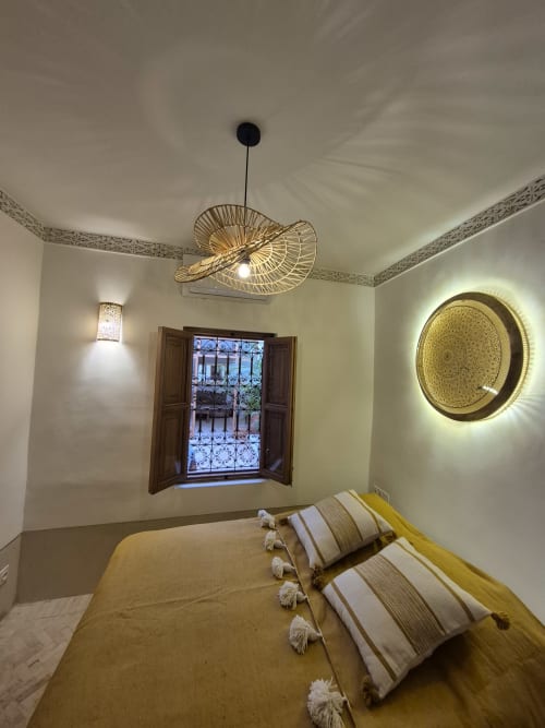 Chambre du Riad Casa Angelo à Marrakech avec lit, ventilateur suspendu, décoration murale, fenêtre cintrée et éclairage chaleureux