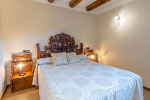 Chambre chaleureuse à l'Hôtel Flor de Neu à El Pont de Suert avec tête de lit sculptée, poutres apparentes et éclairage chaleureux