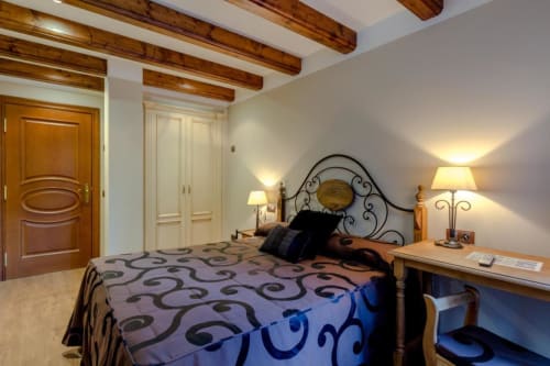 Chambre rustique à l'Hôtel Flor de Neu à El Pont de Suert avec poutres en bois, lit en fer forgé orné et éclairage chaleureux