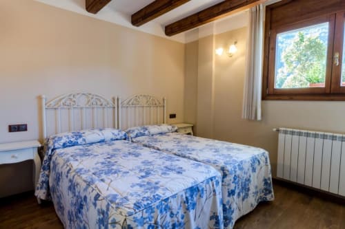 Chambre twin avec literie bleue à fleurs à l'Hôtel Flor de Neu à El Pont de Suert, poutres en bois et vue sur les montagnes