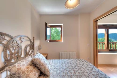 Chambre lumineuse à l'hôtel Flor de Neu avec tête de lit ornementale, vue sur les montagnes et accès à un balcon en bois