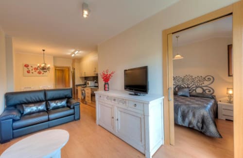 Studio moderne de l'hôtel Flor de Neu avec canapé bleu, télévision, commode blanche et vue sur la chambre, El Pont de Suert