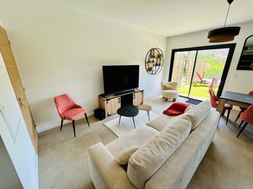 Modern living room in Villa Corail with cream sofa, red chairs, TV, and garden view, managed by Corsu di Core