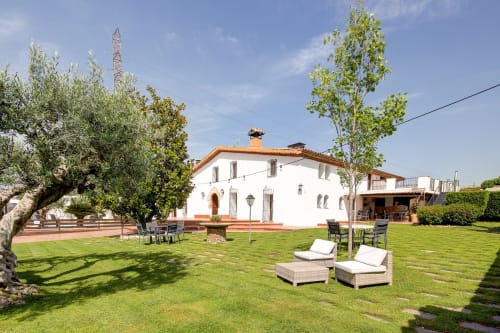 Patio del hotel Masia Can Canyes en Sant Llorenç d'Hortóns con masía blanca, tumbonas, olivo y jardines cuidados