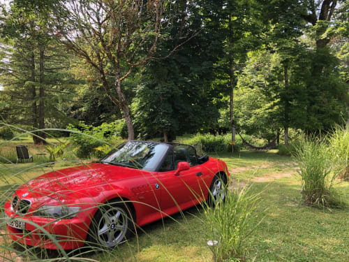 Convertible BMW rojo estacionado en exuberante jardín de Domaine de l'Ocrerie, Pourrain, Francia