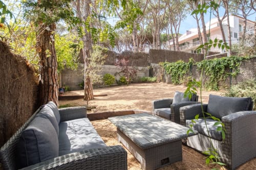 Garden courtyard with rattan seating at Finques Garcia Enrich in Palafrugell, featuring mature trees and outdoor dining area