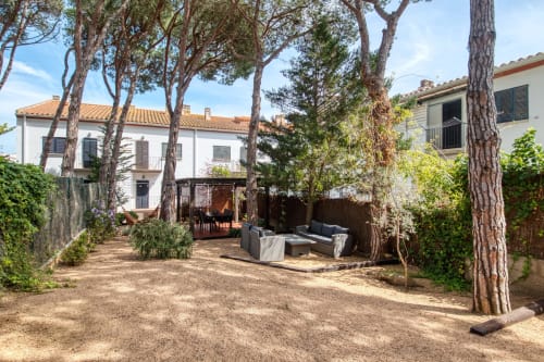 Garden courtyard at Finques Garcia Enrich in Palafrugell with terrace, outdoor seating, tall pine trees and whitewashed