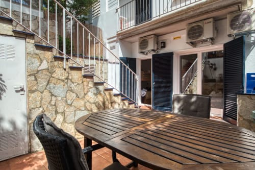 Palafrugell apartment terrace with dining table, stone walls, stairs, and air conditioning units