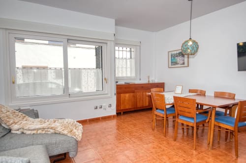 Bright dining room in Palafrugell apartment with wooden table, blue chairs, terracotta tile floor, and large windows