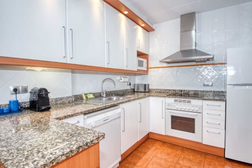 Modern kitchen with white cabinets, granite countertop, stainless appliances, and terracotta floor in Palafrugell apartment