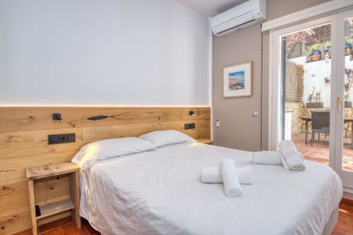 Modern bedroom in Palafrugell apartment with wooden headboard, white bedding, AC unit, and garden view through glass doors