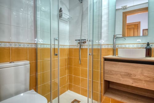 Modern bathroom with orange tiled walls, glass shower enclosure, white sink and toilet at Finques Garcia Enrich, Palafrugell