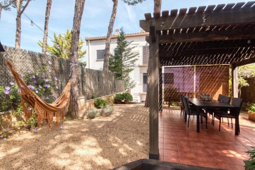 Palafrugell garden apartment with pergola, outdoor dining table, hammock, and stone patio under tall pine trees