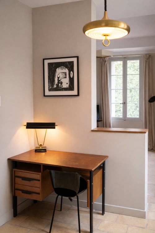 Montpellier B&B workspace: mid-century desk with brass pendant lamp and black chair, framed artwork