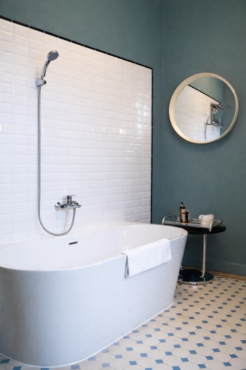 Modern bathroom at Mas De Lafeuillade Montpellier with white tiles, freestanding tub, circular mirror, and blue-gray walls
