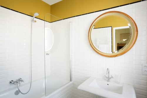 Modern bathroom with yellow walls, round wooden mirror, white sink, and glass shower enclosure at Mas De Lafeuillade in