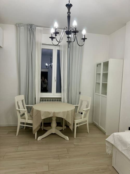 Modernes Esszimmer in den Magnolia Apartments Mailand mit rundem Tisch, weißen Stühlen, schwarzem Kronleuchter und Stadtblick
