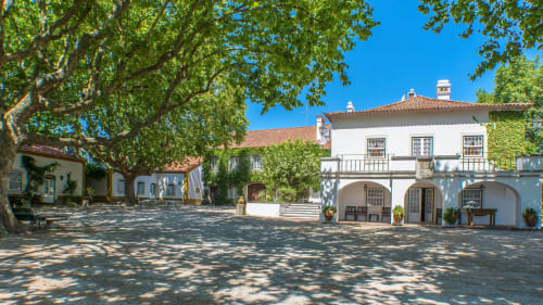 Quinta da Alcaidaria-Mór courtyard in Ourém-Fátima with white colonial buildings, arched portico, and mature shade trees