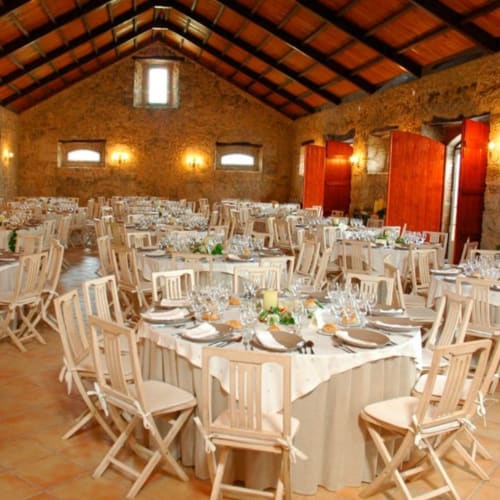 Elegante salão de banquetes na Quinta da Alcaidaria-Mór com mesas redondas, cadeiras de madeira e paredes de pedra rústica em Ourém-Fátima.