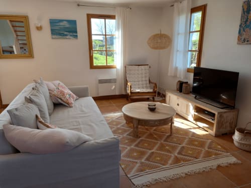Salon lumineux avec canapé confortable, télévision, table ronde et vue sur le jardin à Locmaria Belle Île en Mer
