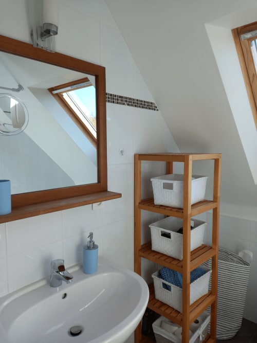 Salle de bain de chalet moderne avec miroir encadré bois, lavabo blanc et étagères bois avec paniers de rangement