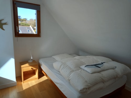 Chambre lumineuse sous les toits avec literie blanche, table de nuit en bois et vue sur les jardins de Belle Île-en-Mer