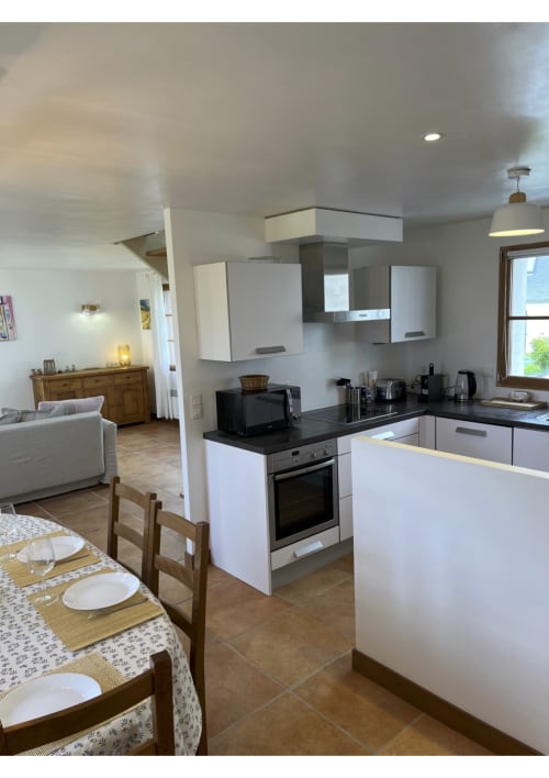 Cuisine ouverte et salle à manger contemporaines du gîte de Belle Île en Mer : meubles blancs, plan de travail noir, table en bois