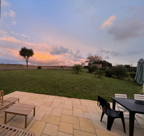 Vue du coucher de soleil depuis la terrasse du gîte Locmaria à Belle Île en Mer, avec salon de jardin et paysage rural