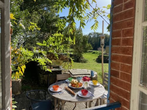 Table de petit-déjeuner en plein air dressée sur la terrasse en brique du cottage de Locmaria, Belle Île en Mer, avec vue sur le jardin