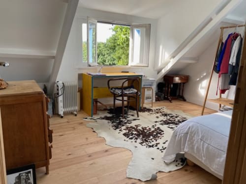 Chambre lumineuse sous les toits avec bureau en bois, portant vêtements, tapis en peau de vache et vue sur le jardin à Locmaria, Belle Île en Mer
