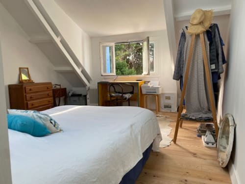 Chambre lumineuse avec lit blanc, meubles en bois, portant, et fenêtre donnant sur le jardin du gîte Loc'Maria, Belle-Île