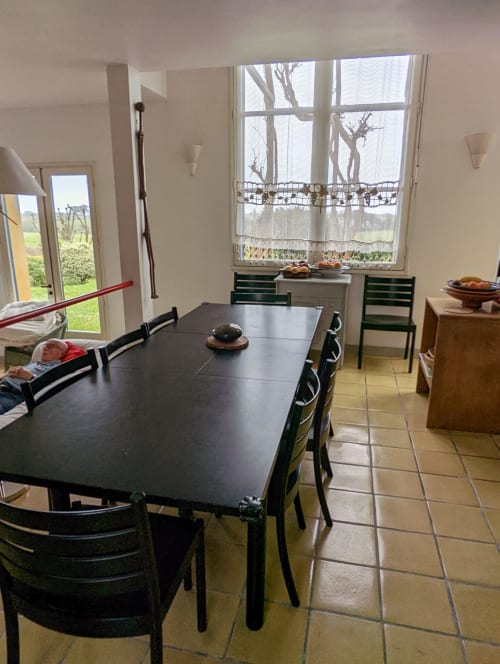 Salle à manger lumineuse avec table et chaises noires, grandes baies vitrées donnant sur les jardins de Belle Île en Mer, cottage de charme