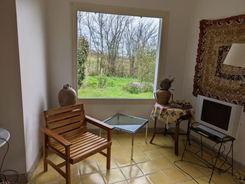 Salon cottage lumineux avec chaise en bois, bureau, télévision et grande fenêtre sur le jardin champêtre de Belle Île