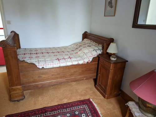 Lit en bois avec édredon décoratif dans une chambre de gîte à Belle Île en Mer, table de nuit avec lampe et tapis