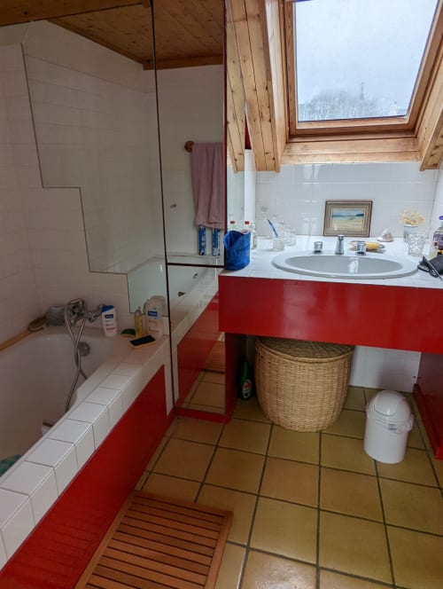 Salle de bain moderne du gîte Belle Île en Mer avec meuble vasque rouge, douche ouverte, vue côtière enneigée et puits de lumière