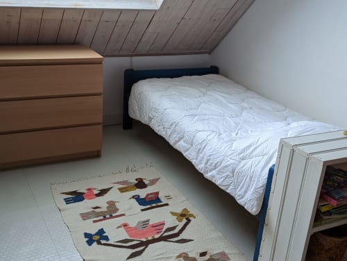 Chambre mansardée du cottage Belle Île avec lit, commode en bois et tapis décoratif à motifs d'oiseaux