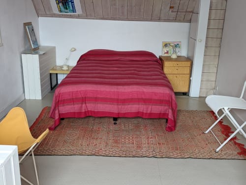 Chambre spacieuse avec literie rayée rouge dans un gîte de Belle-Île-en-Mer. Chaise jaune et mobilier en bois.
