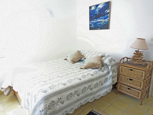 Chambre cosy du gîte Locmaria Belle Île avec tableau marin, literie matelassée, table de nuit en osier et lampe