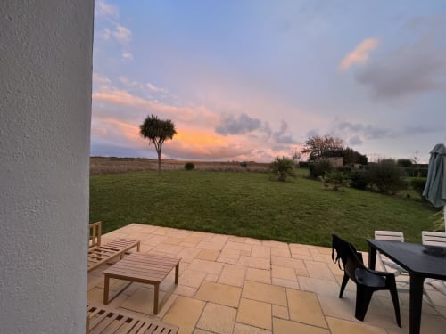 Vue sur le coucher de soleil depuis la terrasse de Belle Île avec palmier, pelouse verte et paysage côtier