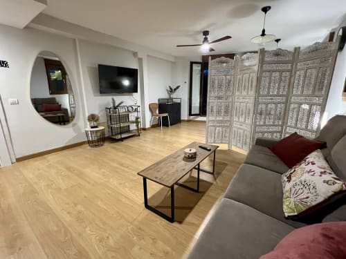 Apartamento moderno en Salamanca con sofá gris, suelos de madera, televisor, biombo decorativo y espejo redondo