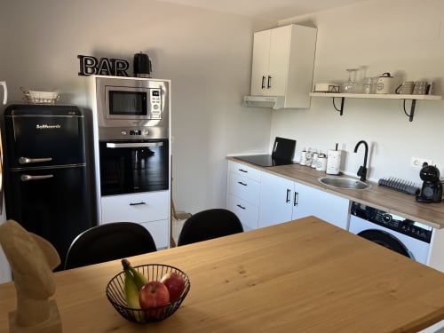 Cocina moderna en apartamento de Salamanca con muebles blancos, mesa de comedor de madera y refrigerador negro vintage