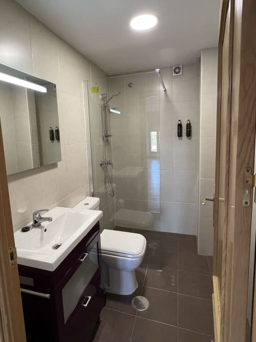 Baño moderno en apartamento AlmaMaterSalamanca con lavamanos doble, ducha con mamparas de vidrio y piso de cerámica oscura