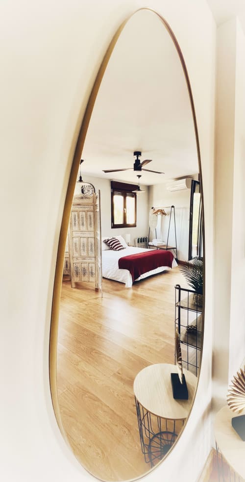 Espejo ovalado reflejando habitación moderna del apartamento en AlmaMaterSalamanca con pisos de madera, ventilador de techo y decoración contemporánea