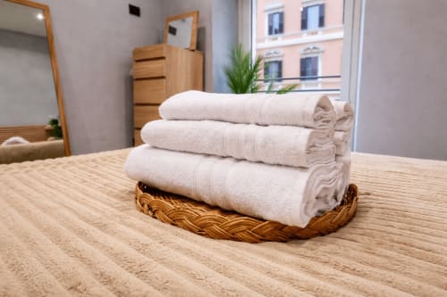Pila di asciugamani bianchi freschi in cesto intrecciato su tavolo di legno all'appartamento Zoelia, Roma
